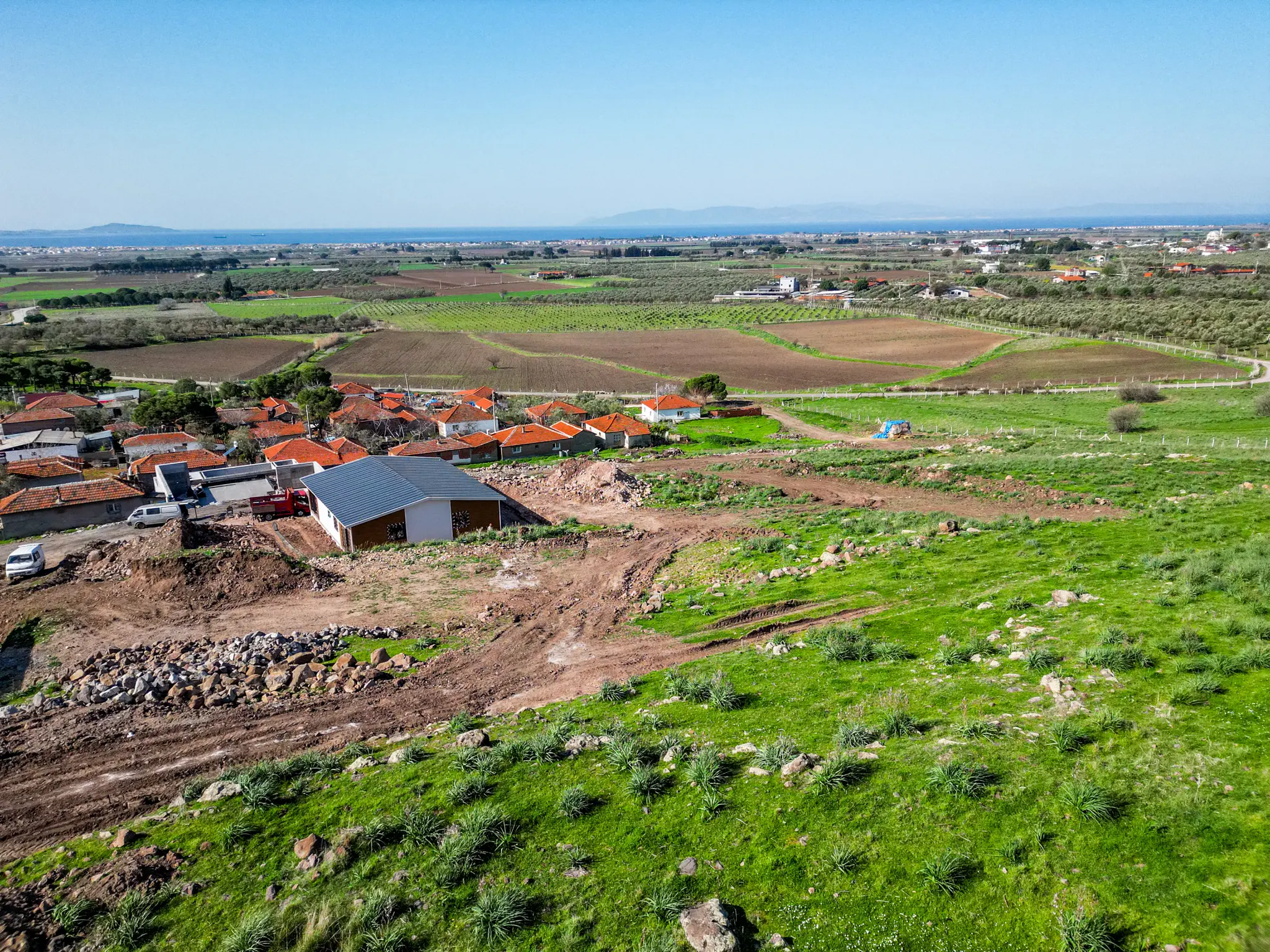 İslamlar Mahallesi'nin yeşil dokusu ve Ege Denizi'ne uzanan manzarasıyla Aqua Dikili proje arazisinin geniş açılı drone fotoğrafı.